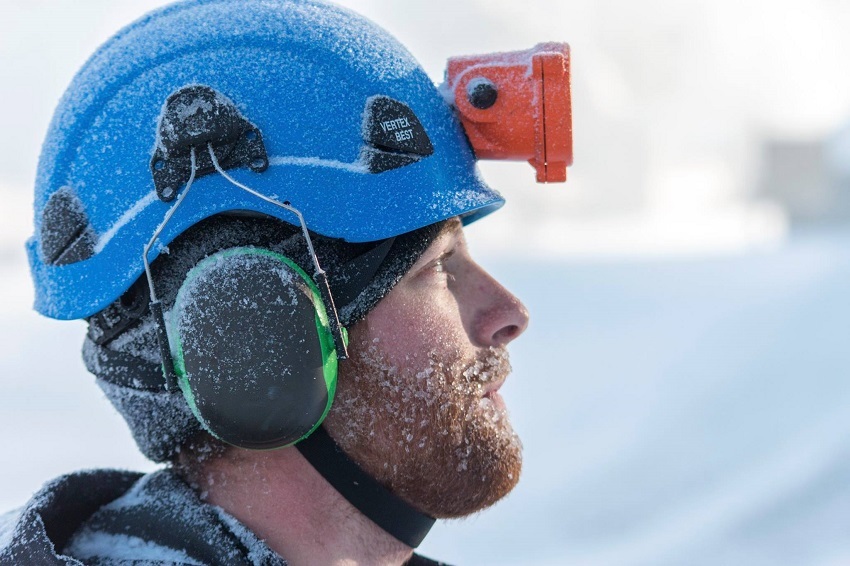Snowmaker with blue helmet, orange headlamp and icy beard