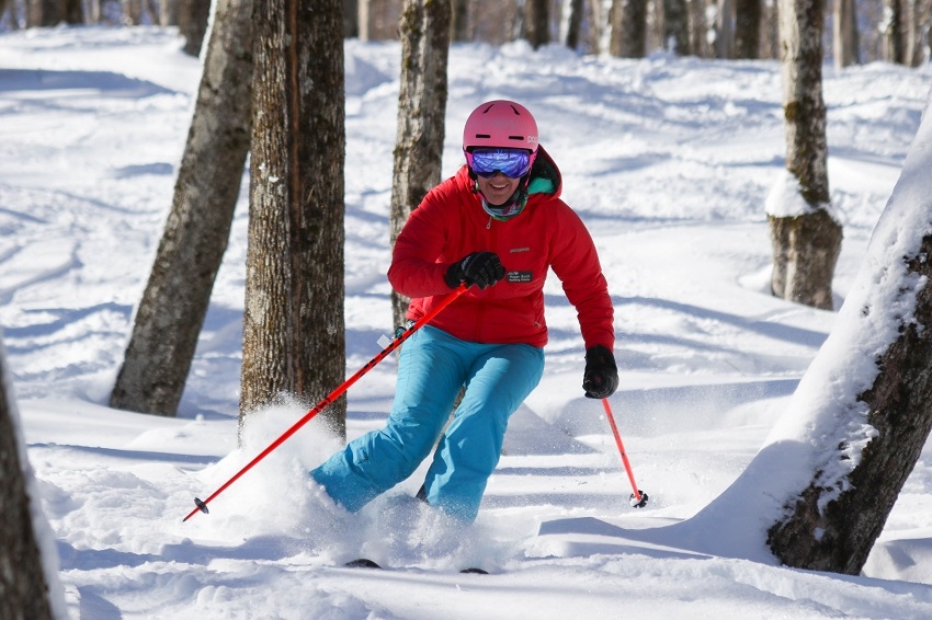 Woman skiing Sunapee woods red jacket blue pants