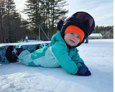Mom holding child with skis toddler with snowboard