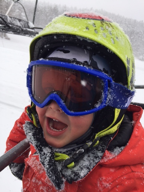 boy on chairlift yellow helmet goggles on snow on jacket